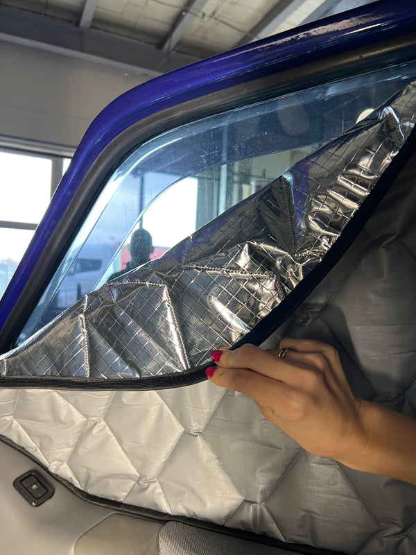 Person holding a reflective car sunshade in front of a vehicle window