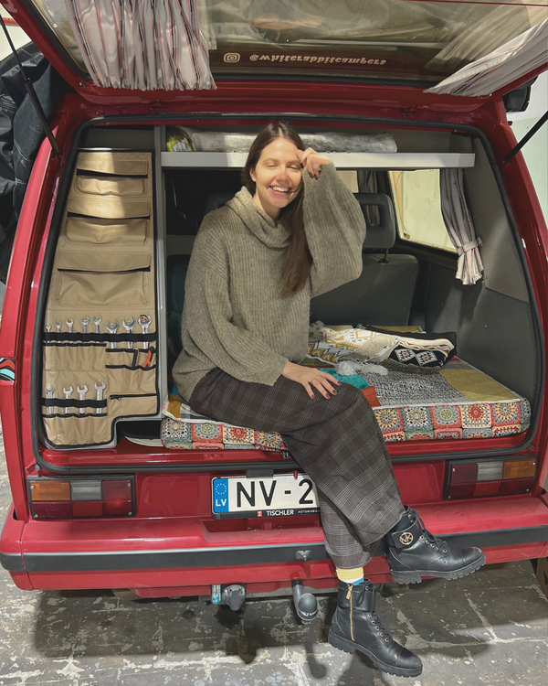 Person sitting inside a red van with camping gear, smiling.